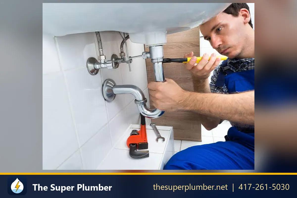 Plumber using a screwdriver on the pipes under a bathroom sink - plumber in Minnesota