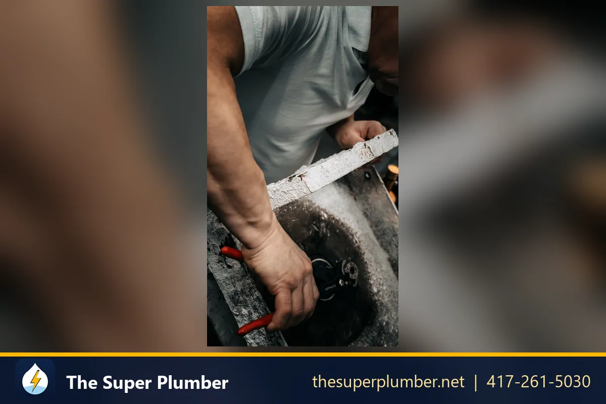 Hands using red-handled pliers on a corroded metal sink basin - best drain cleaner