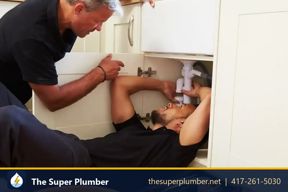 Two plumbers working under a kitchen sink - fix food waste disposer