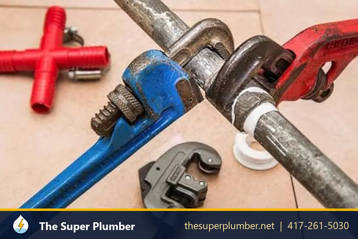 Pipe wrenches gripping a threaded steel pipe beside a tube cutter - plumbing installation