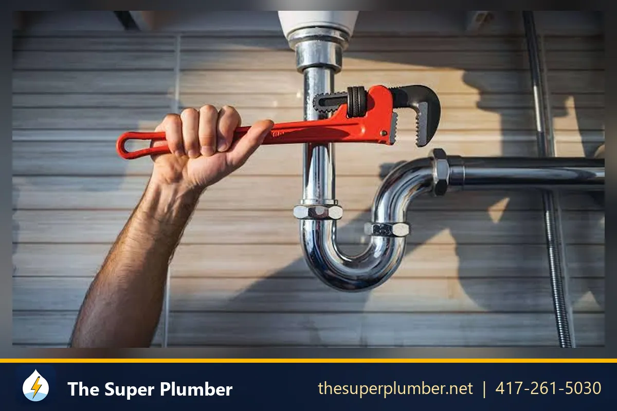 Hand using a red pipe wrench on a chrome P-trap under a sink - sewer drain cleaning