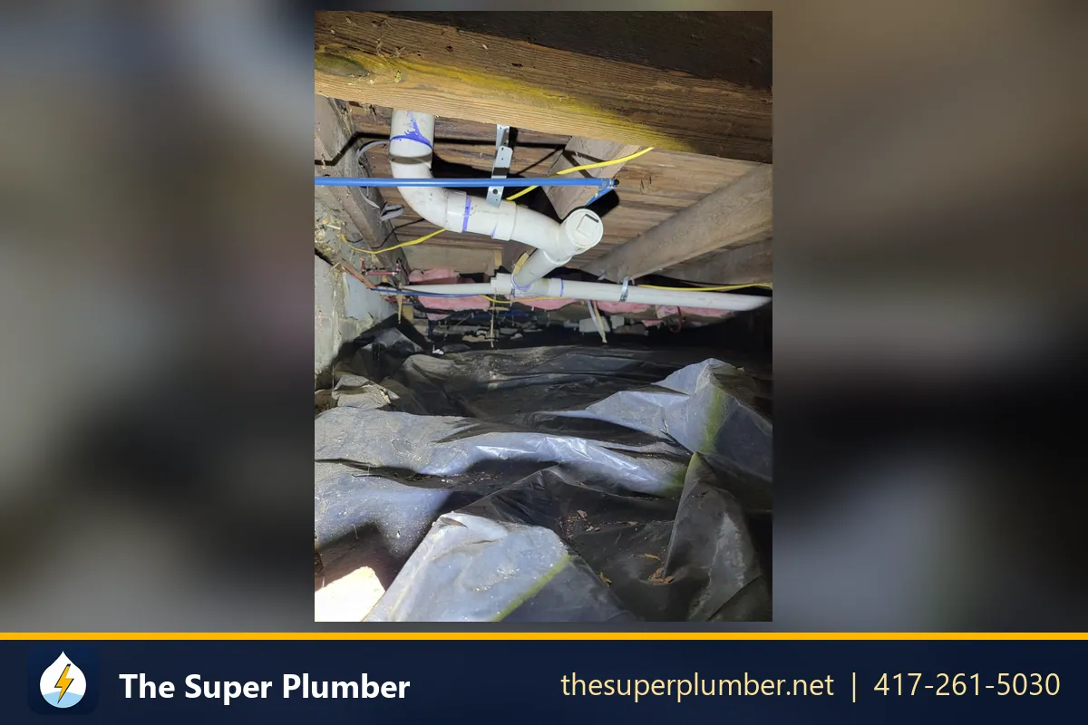White PVC drain pipes and supply lines under floor joists above a plastic-lined crawlspace - water leak repair